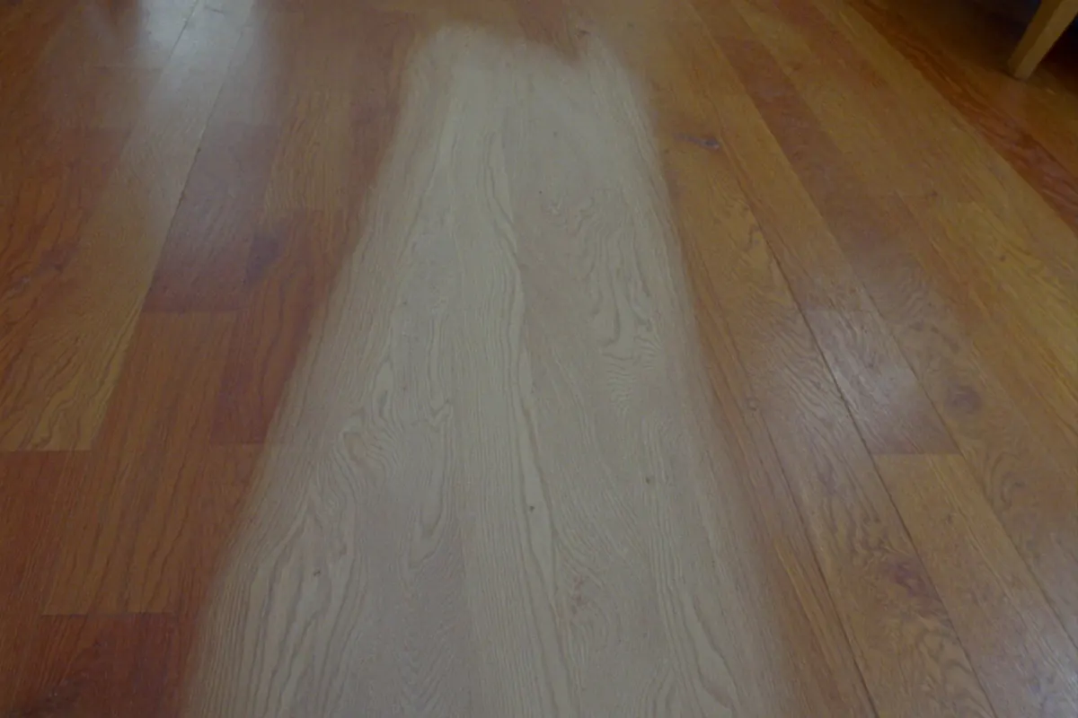 A pale walking path worn through the finish of an oak floor, with the surrounding boards still amber